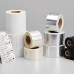 Thermal label rolls in paper, polypropylene, and polyester materials beside thermal transfer ribbon rolls